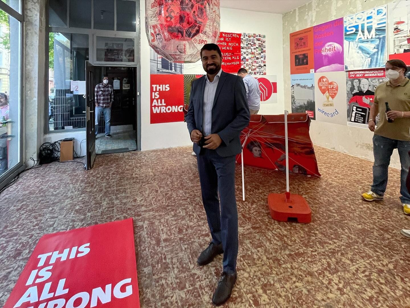 «Die Zukunft der SPD #2» — Serdar Yüksel (Vorsitzender SPD Bochum) im Ausstellungsraum mit «THIS IS ALL WRONG» und Sonnenschirm