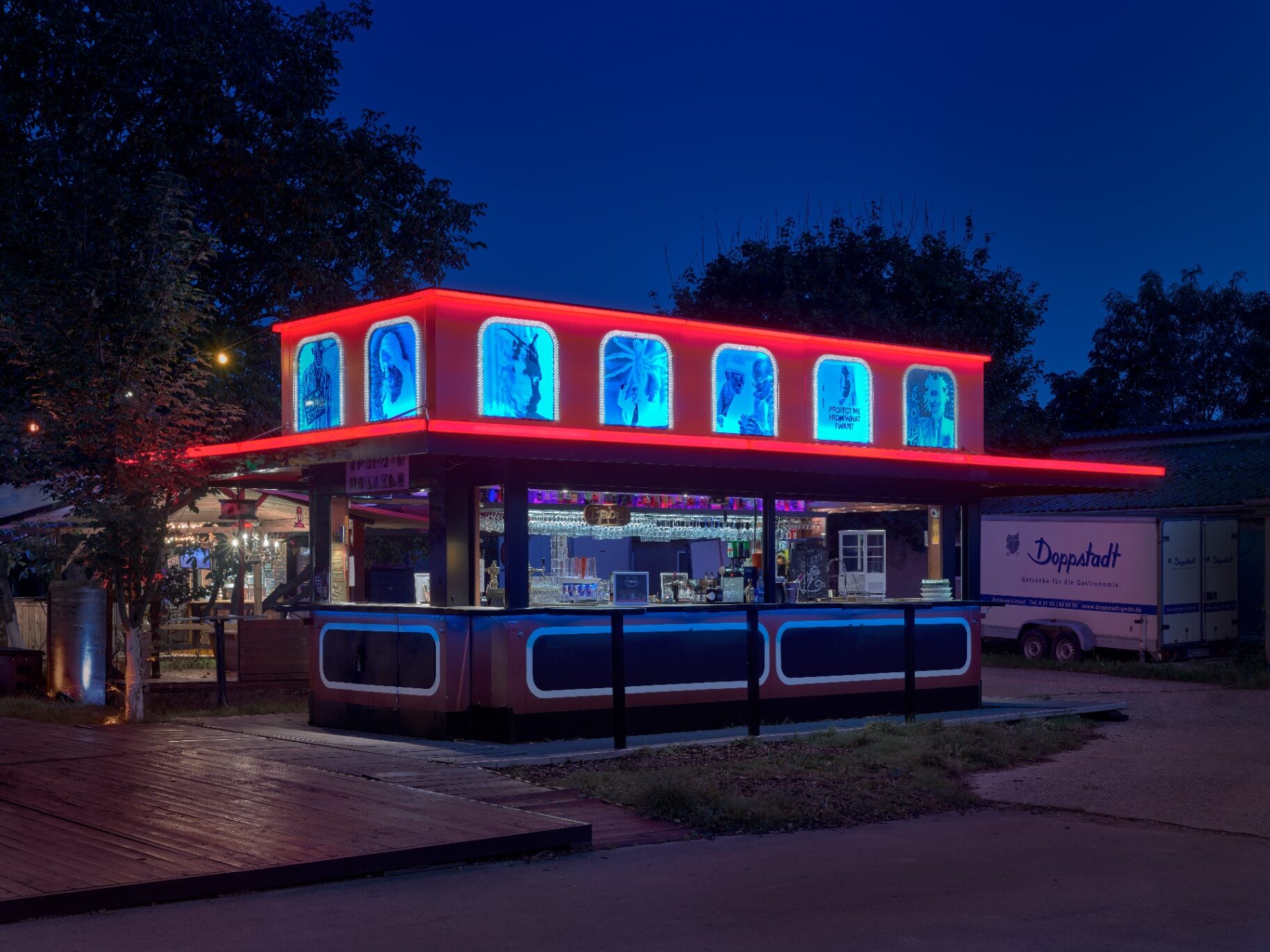 «Kirmeswagen» — Frontansicht bei Nacht mit roter Neonumrandung und sieben beleuchteten Porträtnischen