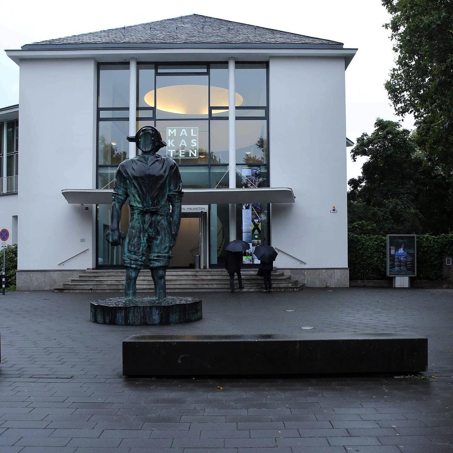 «Malkasten revisited» — Vorplatz mit Bronze-Skulptur und Besuchern vor dem Eingang